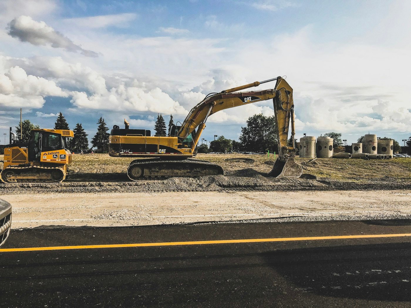 Excavators grading the roadbed beside a freshly paved road on a municipal infrastructure project